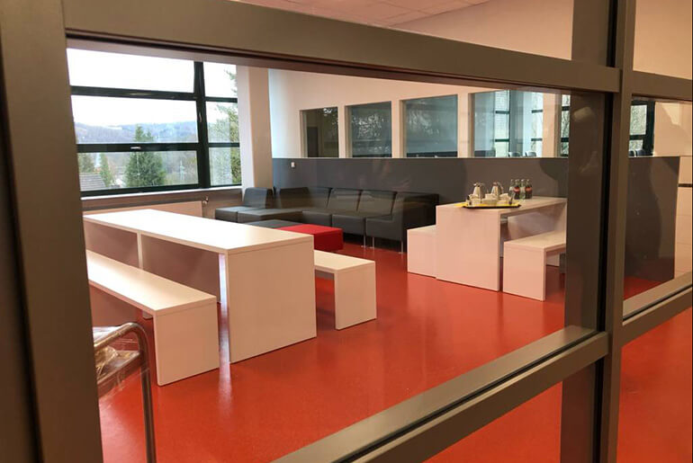 Modern eingerichteter Besprechungsraum für Schülerinnen und Schüler mit weißen Möbeln, schwarzen Sitzgelegenheiten und einem orangenen Boden