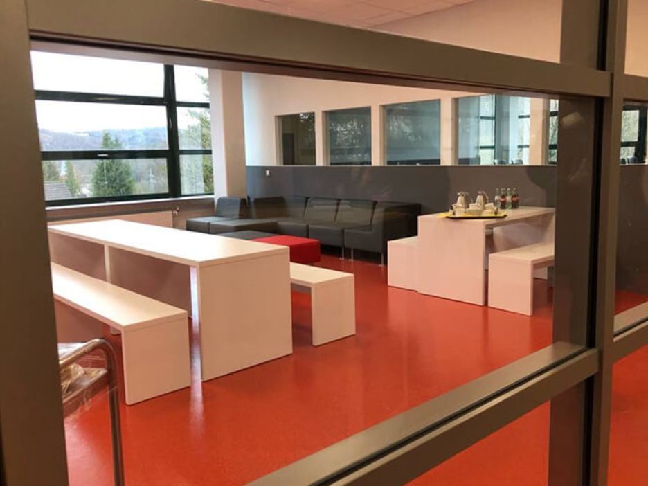 Modern eingerichteter Besprechungsraum für Schülerinnen und Schüler mit weißen Möbeln, schwarzen Sitzgelegenheiten und einem orangenen Boden