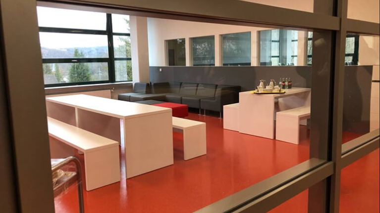 Modern eingerichteter Besprechungsraum für Schülerinnen und Schüler mit weißen Möbeln, schwarzen Sitzgelegenheiten und einem orangenen Boden