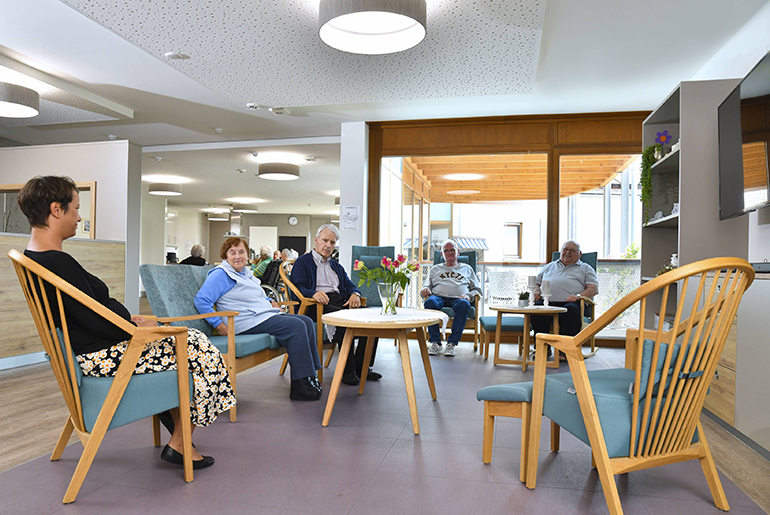 Alte Menschen sitzen in einer Holz-Sitzgruppe mit türkisen Polstern.