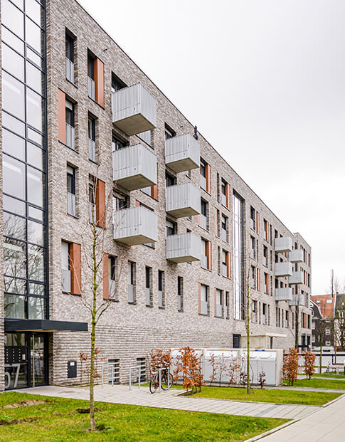 Hausfront einer modernen Wohnanlage mit Vorgärten und Fahrradständer am Eingang