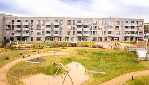 Hausfront einer modernen Wohnanlage, davor eine große Grünfläche mit Spielplatz
