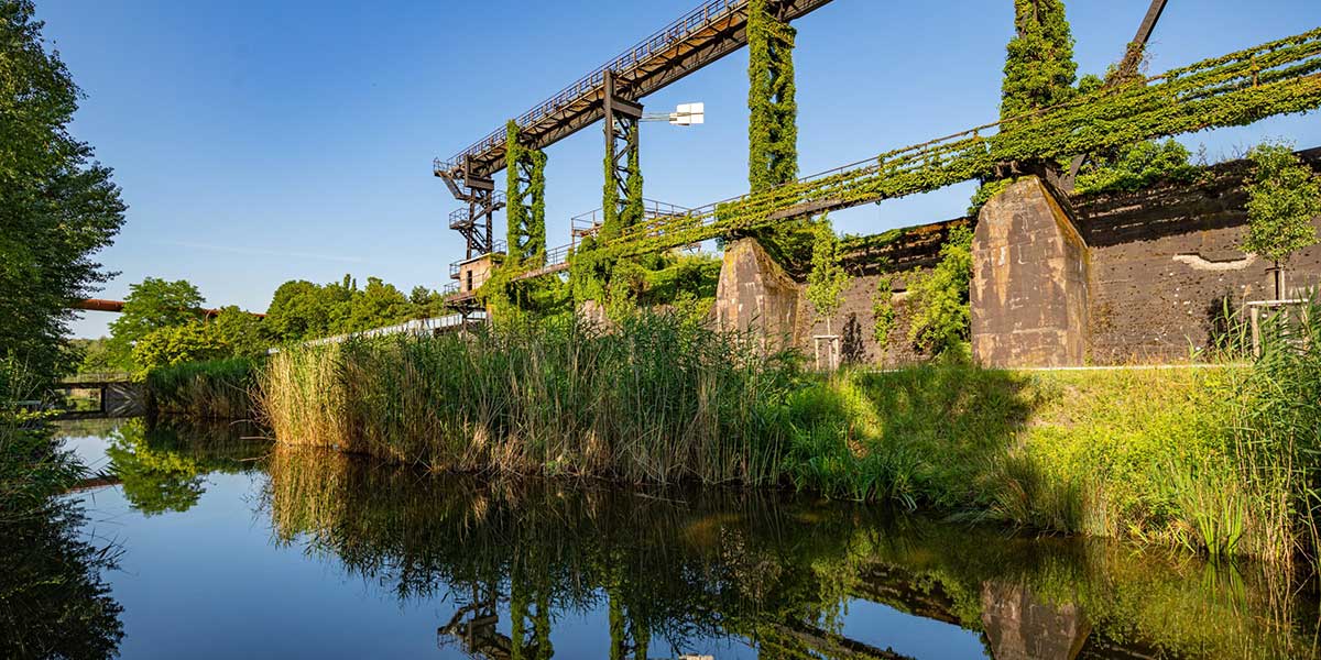 Am Ufer der renaturierten Emscher steht ein begrüntes Industriedenkmal.