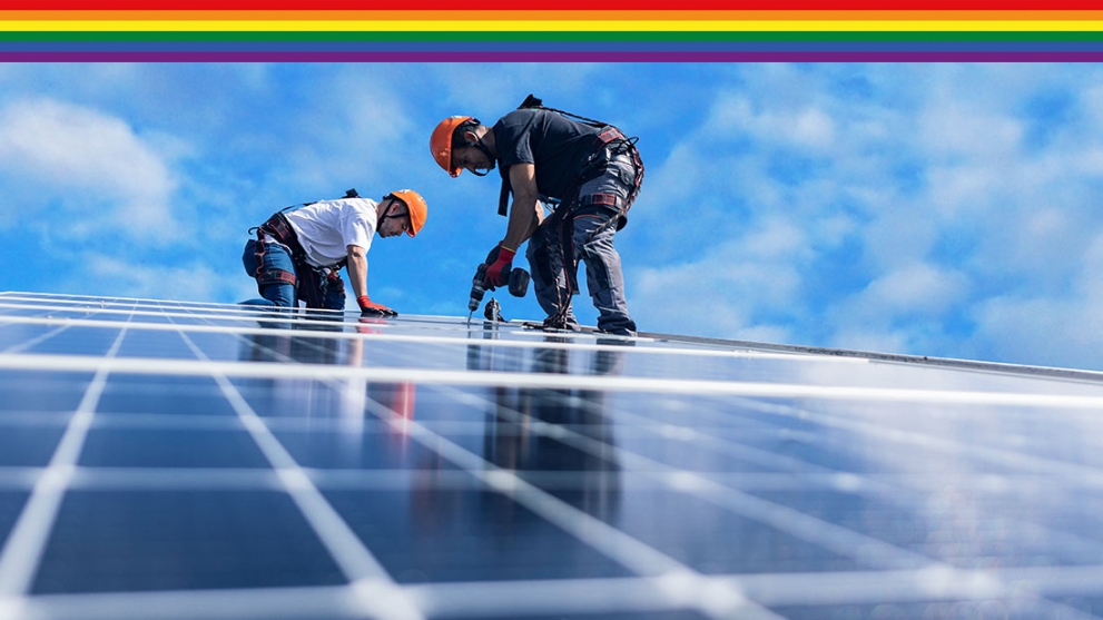 Zwei Männer mit orangenen Helmen befestigen mit einer Bohrmaschine Solarpaneele auf einem Dach´.