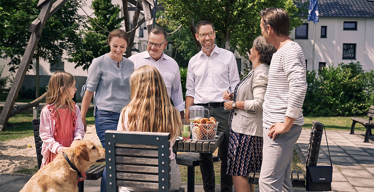 Zwei Männer, eine Frau, zwei Mädchen und ein Hund beim Picknick im Freien an einem Holztisch