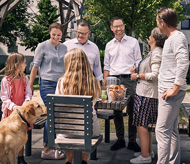 Zwei Männer, eine Frau, zwei Mädchen und ein Hund beim Picknick im Freien an einem Holztisch