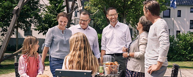 Zwei Männer, eine Frau, zwei Mädchen und ein Hund beim Picknick im Freien an einem Holztisch