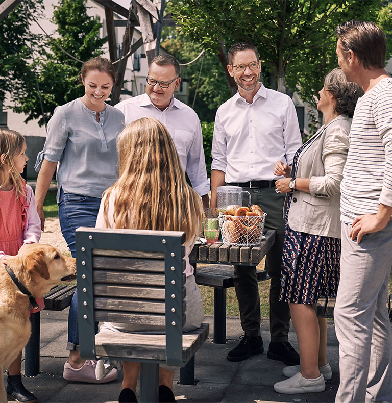 Zwei Männer, eine Frau, zwei Mädchen und ein Hund beim Picknick im Freien an einem Holztisch