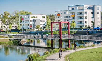 Der Niederfeldsee in Essen mit Radwegen und viel Grün, dahinter ein moderner Wohnkomplex