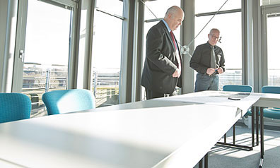 Zwei Männer stehen in einem hellen Konferenzraum mit bodentiefen Fenstern