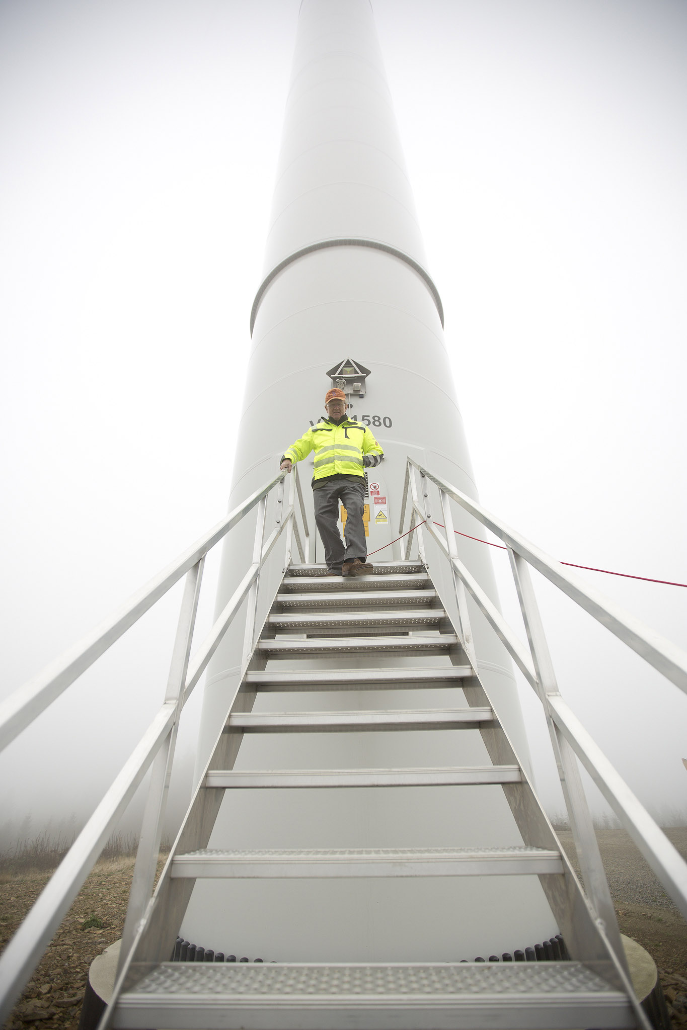 Mann in neongelber Jacke kommt die Treppe am Fuße eines Windrades herunter