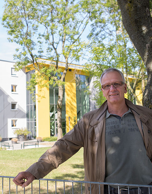 Ein Mann steht im Garten vor einem modern sanierten Mehrfamilienhaus.