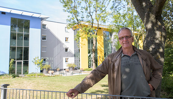 Ein Mann steht im Garten vor einem modern sanierten Mehrfamilienhaus.