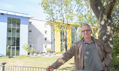 Ein Mann steht im Garten vor einem modern sanierten Mehrfamilienhaus.