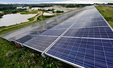 Großflächige Solaranlage auf einer Wiese, im Hintergrund ein kleiner See