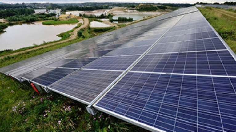 Großflächige Solaranlage auf einer Wiese, im Hintergrund ein kleiner See