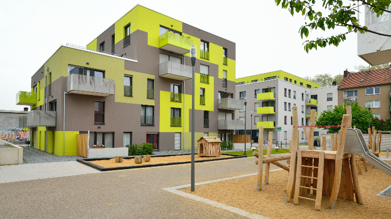 Modernes Wohnquartier mit gelb-grauer Fassade, davor ein Spielplatz