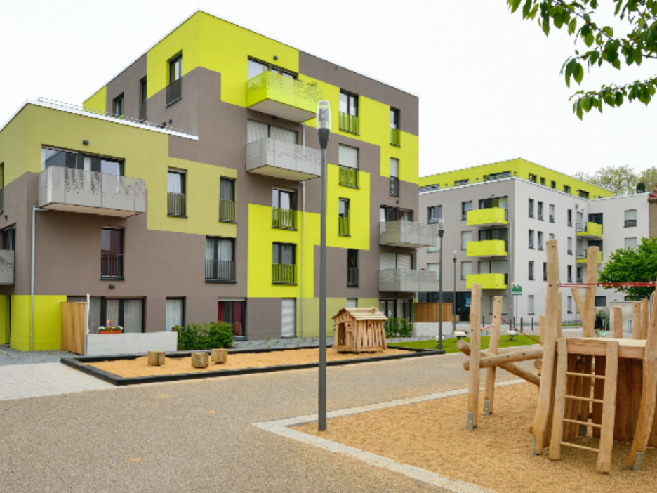 Modernes Wohnquartier mit gelb-grauer Fassade, davor ein Spielplatz