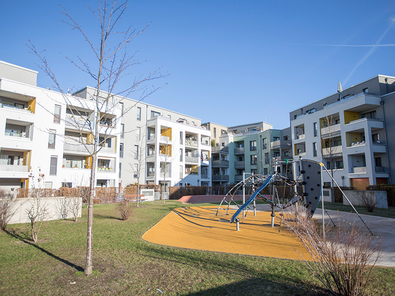 Das Carlswerkquartier in Köln: heller, moderner Wohnblock, davor ein Park mit Spielplatz