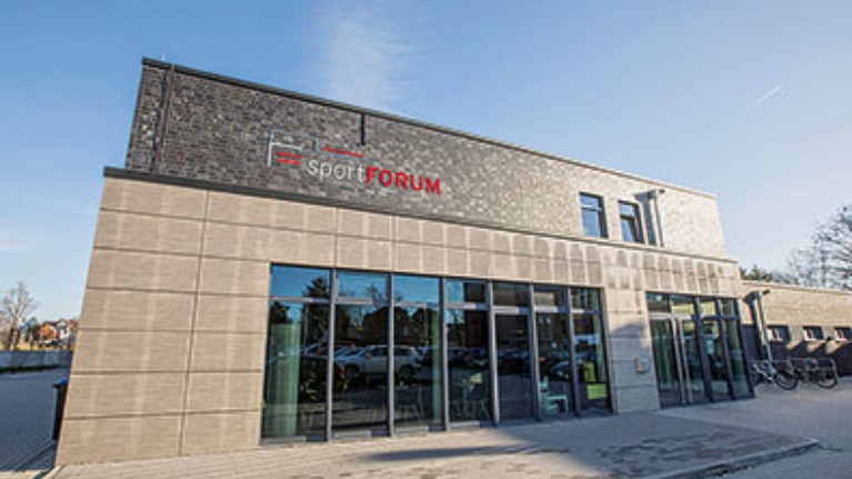 Außenansicht des sportFORUMs Rheine: Graue Fassade, Fensterfront und Schriftzug Sport Forum