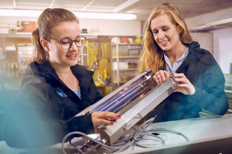 Zwei junge Frauen inspizieren in einer Werkstatt ein elektrisches Bauteil.