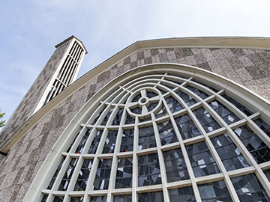 Graue Stein-Fassade einer Kirche mit geschwungener Fensterfront aus der Froschperspektive