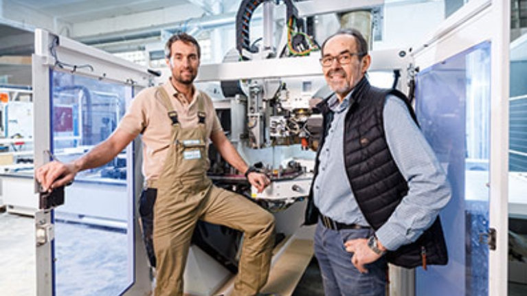 Jan und Josef Hüser, Geschäftsführer der Hüser Michels GmbH, vor einer großen Maschine in ihrer Firma