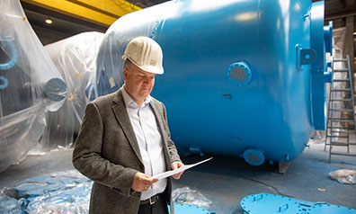 Dr. Jörg Doege, Geschäftsführer von Inprocoat, mit Schutzhelm vor einem Metalltank in einer Werkshalle