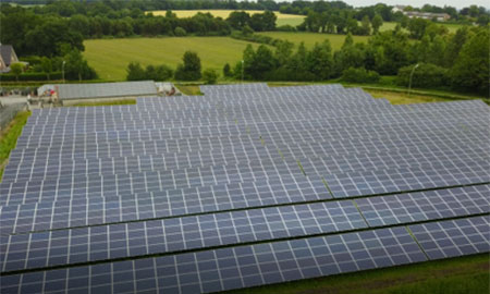 Großflächige Solaranlage auf einer Wiese. Im Hintergrund Felder und Bäume