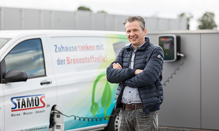 Ein Mann vor einem Elektro-Lieferwagen der Firma Stamos. Dieser wird gerade geladen.