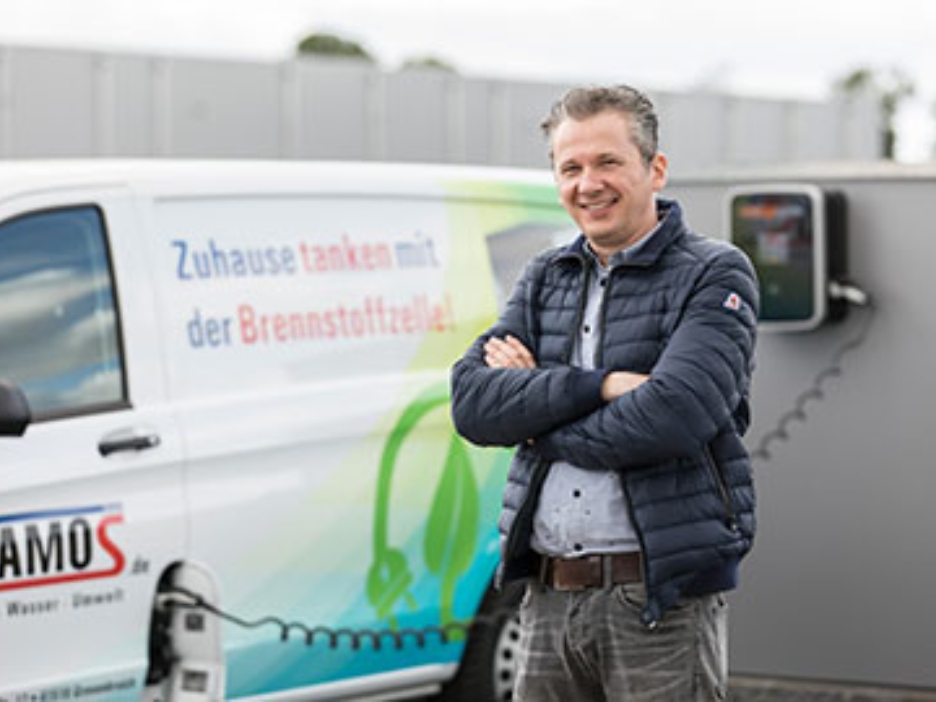 Ein Mann vor einem Elektro-Lieferwagen der Firma Stamos. Dieser wird gerade geladen.