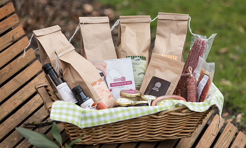 Ein Picknickkorb mit Lebensmitteln der Marke Bauernbox steht auf eine Parkbank.