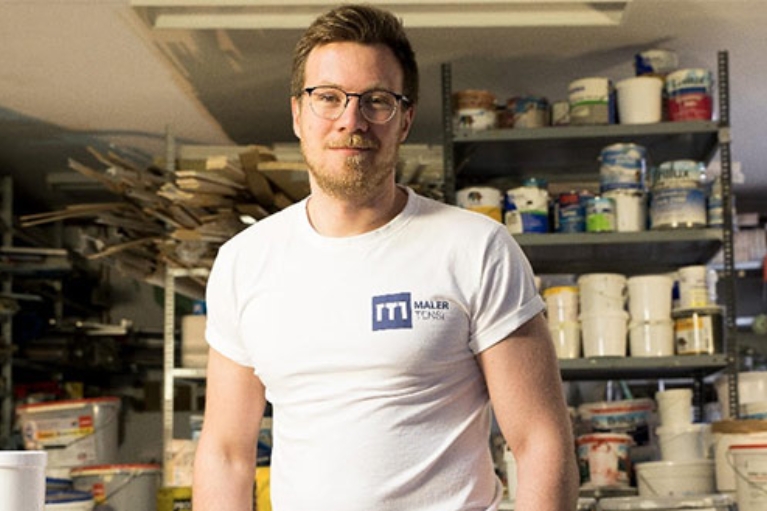 Malermeister Marc Tensi weiß gekleidet in seinem Materiallager