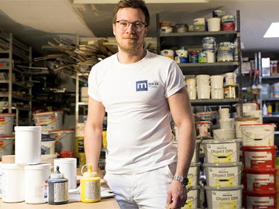 Malermeister Marc Tensi weiß gekleidet in seinem Materiallager
