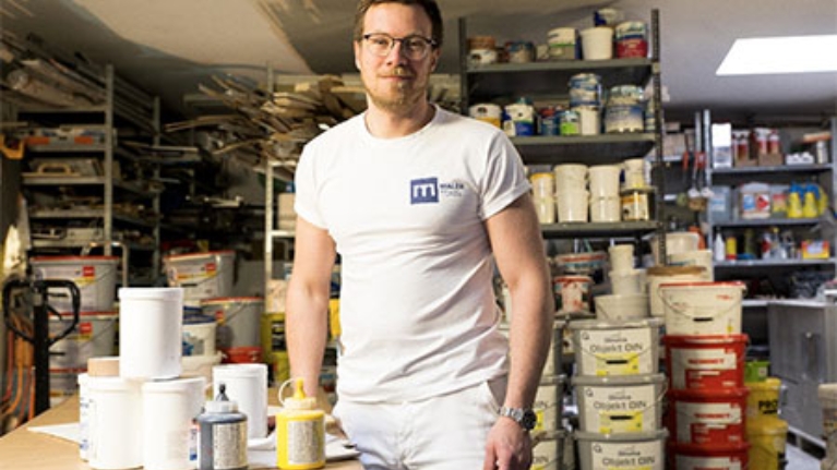 Malermeister Marc Tensi weiß gekleidet in seinem Materiallager