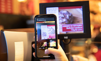 Display einer modernen Kasse, davor ein Smartphone, welches den Code auf dem Display scannt