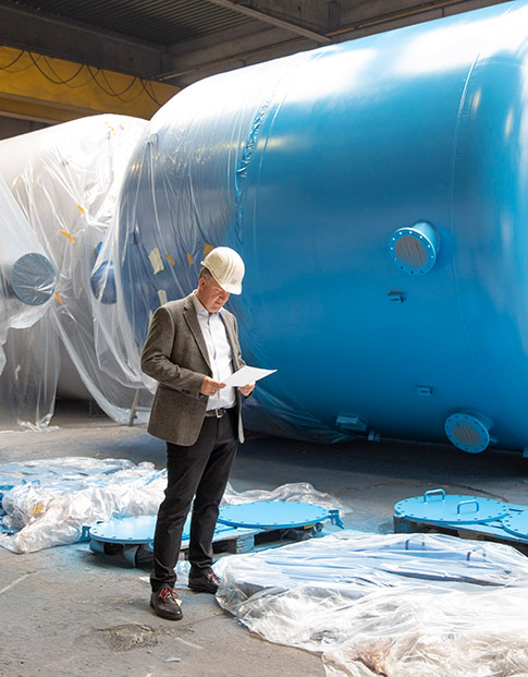 Dr. Jörg Doege, Geschäftsführer von Inprocoat, mit Schutzhelm vor einem Metalltank in einer Werkshalle