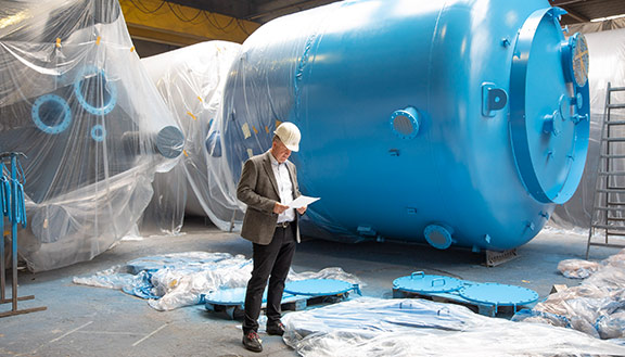 Dr. Jörg Doege, Geschäftsführer von Inprocoat, mit Schutzhelm vor einem Metalltank in einer Werkshalle