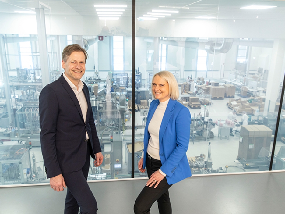 Babor-Geschäftsführer Stefan Kehr war Claudia Brendt von der Förderberatung Rheinland stehen vor einer scheibe, die den Produktionsbereich abtrennt