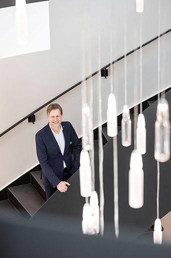 Babor-Geschäftsführer Stefan Kehr steht in einem treppenhaus, von deren Decke viele kleine Ampullen hängen, die als Lampe dienen