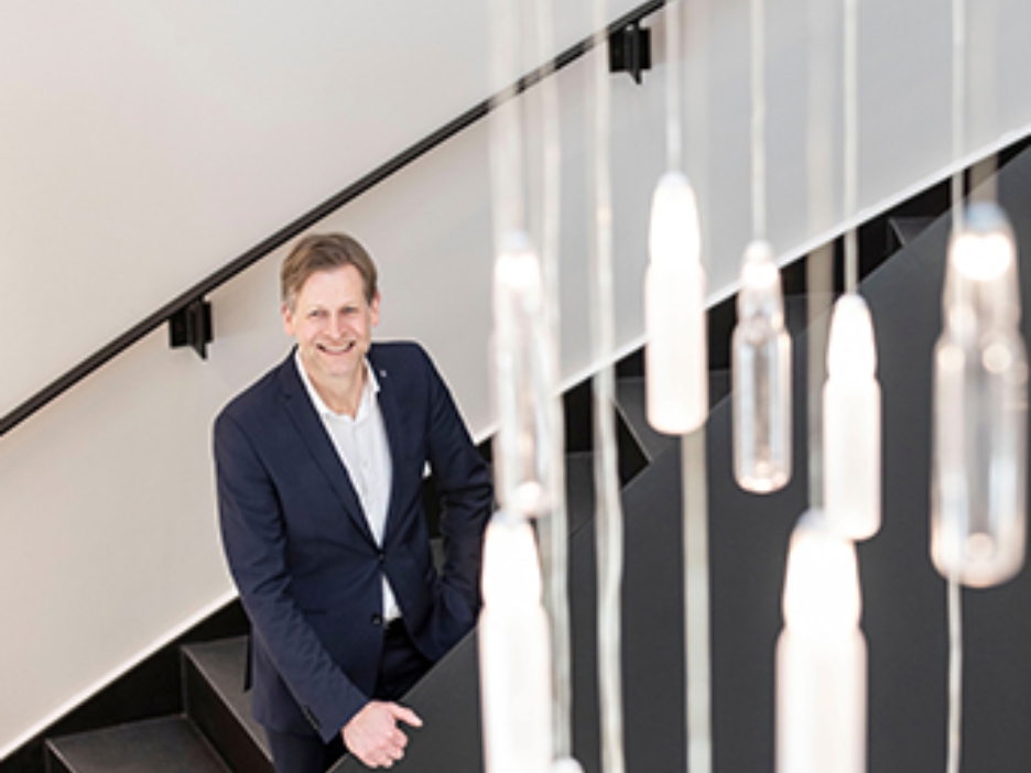 Babor-Geschäftsführer Stefan Kehr steht in einem treppenhaus, von deren Decke viele kleine Ampullen hängen, die als Lampe dienen