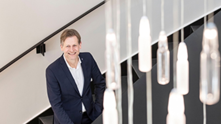 Babor-Geschäftsführer Stefan Kehr steht in einem treppenhaus, von deren Decke viele kleine Ampullen hängen, die als Lampe dienen