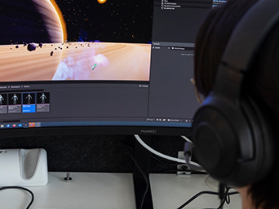 PC Bildschirm an dem ein Mann mit Kopfhörern sitz und programmiert