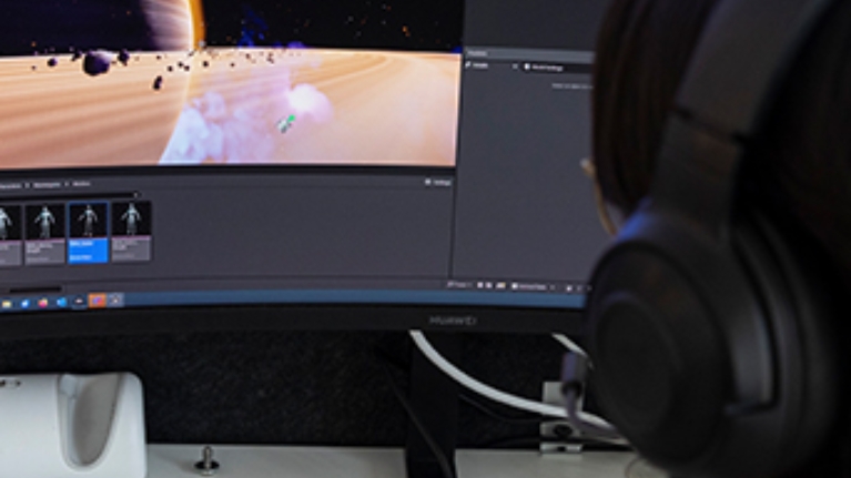 PC Bildschirm an dem ein Mann mit Kopfhörern sitz und programmiert