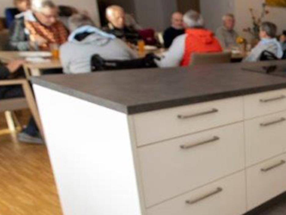 Eine Kochinsel steht in einem Speiseraum mit mehreren älteren Menschen