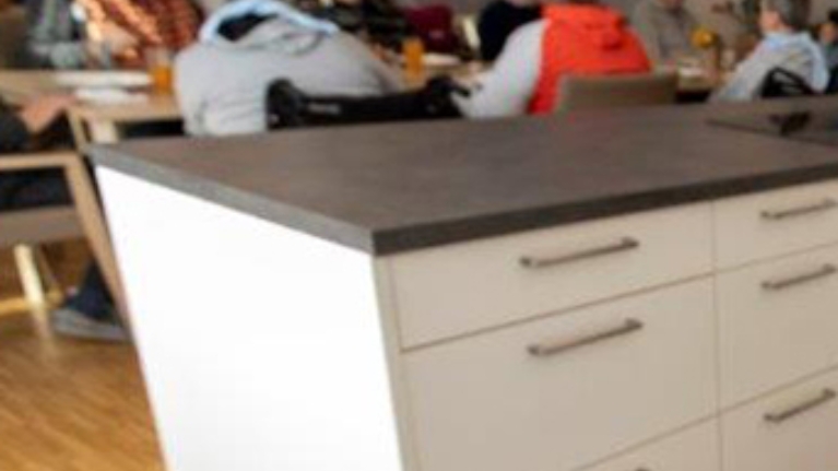 Eine Kochinsel steht in einem Speiseraum mit mehreren älteren Menschen