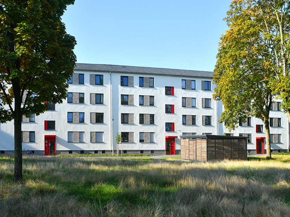 Ein großflächiges Mietshaus mit weißer Fassade und roten Türelementen im Grünen