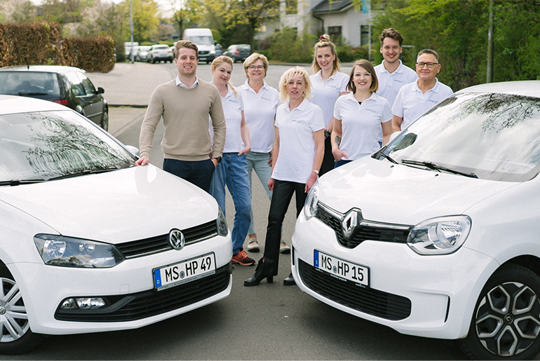 Das Team von Home Plus steht zwischen zwei Autos aus ihrem Fuhrpark