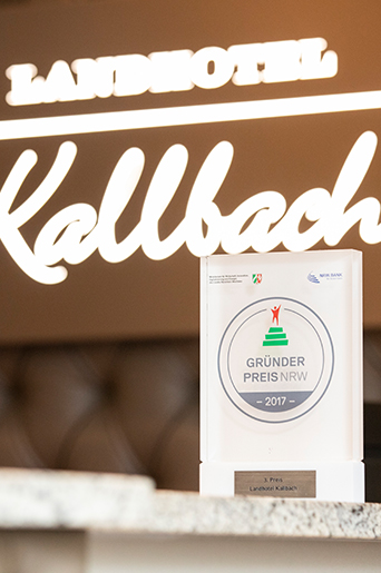 Die Trophäe des 2017 gewonnenen GRÜNDUNGSPREIS NRW steht vor dem Logo des Hotels Kallbach