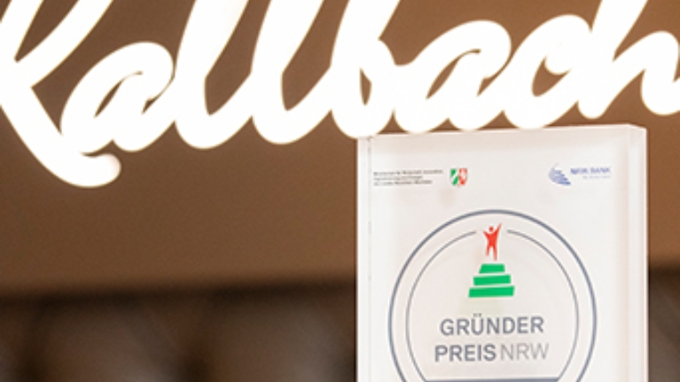 Die Trophäe des 2017 gewonnenen GRÜNDUNGSPREIS NRW steht vor dem Logo des Hotels Kallbach